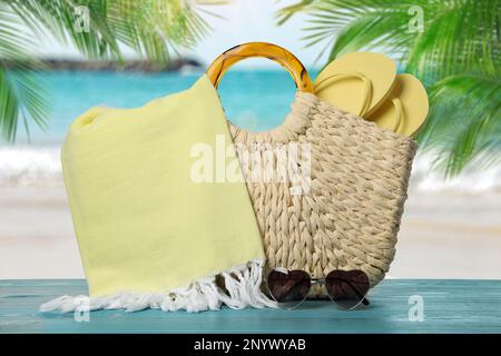 Borsa da spiaggia con asciugamano, infradito e occhiali da sole a forma di cuore su superficie di legno blu chiaro vicino al mare Foto Stock