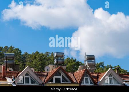 Tetto a tegole di una casa con stoviglie satellitari e vasche per il riscaldamento dell'acqua. Cielo blu con nuvole bianche chiaro. Foto Stock