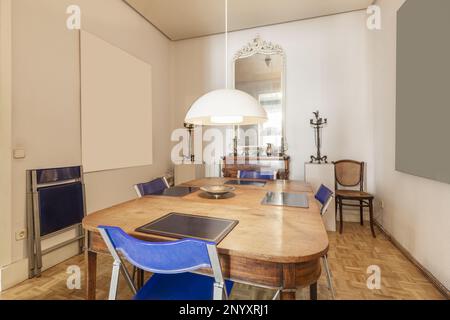 Sala da pranzo di una casa con un tavolo in legno vintage e sedie pieghevoli in plastica blu e metallo in una stanza con pavimenti in parquet di quercia Foto Stock