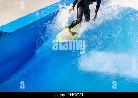 Un surfista godendo le creste delle onde in una piscina urbana a onde nella sua muta nera Foto Stock