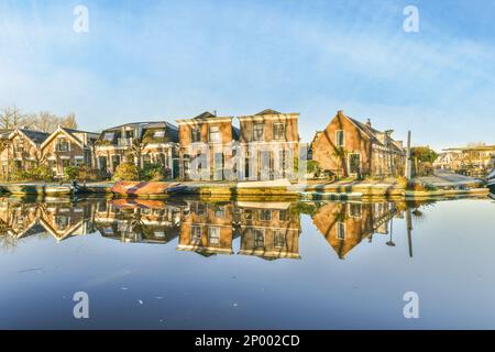Amsterdam, Paesi Bassi - 10 aprile 2021: Alcune case e barche in acqua in una giornata di sole con il cielo blu riflesso nella superficie ancora calma delle acque Foto Stock