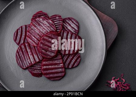Deliziose e sane barbabietole bollite di colore rubino affettate su un piatto nero su uno sfondo di cemento scuro Foto Stock