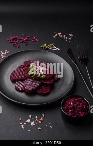 Deliziose e sane barbabietole bollite di colore rubino affettate su un piatto nero su uno sfondo di cemento scuro Foto Stock