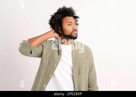 Un curly afroamericano perplesso che tiene la mano sulla parte posteriore della testa in piedi isolato su bianco perso nei dubbi, l'uomo immerso nel pensare o nel prendere decisioni importanti, risolvendo il problema Foto Stock