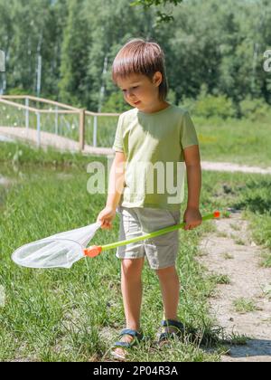 Il bambino piccolo cammina all'aperto con la rete delle farfalle. Attività estiva per i bambini. Caccia agli insetti. Foto Stock