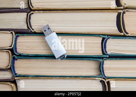 Unità flash USB di un computer sullo sfondo di una pila di vecchi libri di carta. Confronto di volumi di supporti di archiviazione di epoche diverse Foto Stock