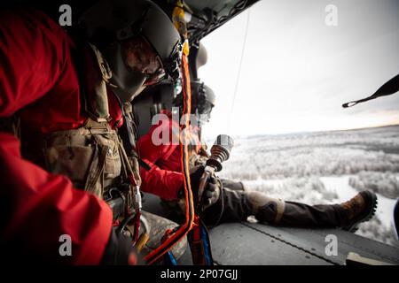 Matthew Tucker, una medica di volo assegnata a Golf Company, distaccamento 2, 2-211th General Support Aviation Battalion, si prepara ad essere abbassato tramite un paranco da un elicottero Black Hawk dell'Alaska Army National Guard HH-60m a Camp Mad Bull su Joint base Elmendorf-Richardson, Alaska, 10 gennaio 2023. Gli equipaggi della Guardia militare hanno condotto operazioni di inserimento aereo, evacuazione medica e sollevamento con gli Airmen Special Tactics, assegnati a 24th Special Operations Wing, distaccamento 1. Il battaglione di aviazione generale di supporto della Guardia Nazionale dell'Alaska si allena regolarmente con tutti i rami della miliita Foto Stock