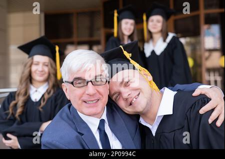 Padre e figlio si abbracciano alla laurea. Il genitore si congratula con il laureato. Foto Stock