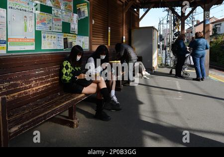 Giovani donne giapponesi sedute su una vecchia panca di legno alla stazione ferroviaria di Kamakura, Giappone. Foto Stock