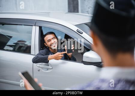 uomo in auto che mostra il telefono cellulare a un uomo con tappo Foto Stock