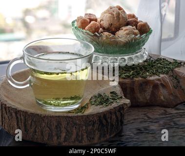 Rinfrescati e gusta una tazza di tè alla canapa calda (tè alle erbe del CBD) servito con focaccine e crostini su un vecchio tavolo rustico in legno vicino alla finestra con su Foto Stock