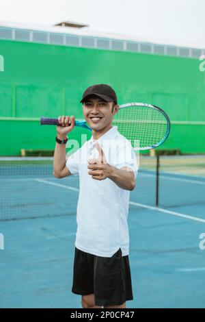 atleta sorridente con i pollici in su mentre trasporta la racchetta Foto Stock