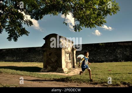 Un bambino corre mentre sta giocando a calcio su un campo d'erba dove un cimitero europeo è stato collocato vicino a Fort Speelwijk, un forte olandese costruito nel territorio di Banten Sultanato in un'area ora chiamata Banten lama (Old Banten) a Serang, Banten, Indonesia, in questa foto scattata nel 2010. Una ricerca sul campo condotta recentemente da Nurikah e E. Rakhmat Jazuli (Facoltà di giurisprudenza, Sultan Ageng Tirtayasa University, Banten) ha rivelato che ci sono state molte violazioni contro il trattamento dei beni culturali nella zona. Le persone "svolgono attività sportive nell'ambiente dei beni culturali, Foto Stock