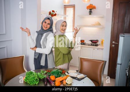 due donne in hijab con gesto della mano che si presenta durante la cottura Foto Stock