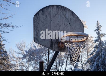 Questa immagine mostra un primo piano astratto vista a basso angolo di un vecchio grungy canestro da basket all'aperto e cangboard, contenente neve da una recente Blizzard con Foto Stock