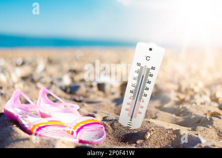 estate tempo e sentire concetto, termometro in sabbia sulla spiaggia contro il mare e cielo blu Foto Stock