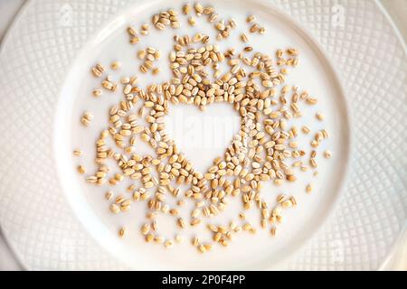 Pearl barley grain in a shape of heart spilled on a plate. Raw groats food ingredient background. Love for cooking concept Stock Photo