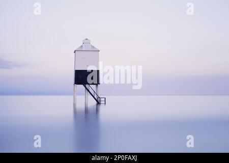 Vista del faro a basso palo di legno sulla spiaggia durante la marea crescente all'alba, durante una delle maree più alte per un decennio, faro basso (faro acceso Foto Stock