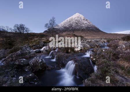 Vista della brughiera con piccole cascate in torrente roccioso e montagna innevata sullo sfondo all'alba, Stob Dearg, Buachaille Etive Mor, Glen Etive Foto Stock