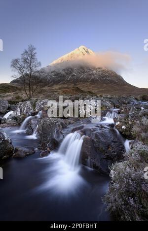 Vista della brughiera con piccole cascate in torrente roccioso e montagna innevata sullo sfondo all'alba, Stob Dearg, Buachaille Etive Mor, Glen Etive Foto Stock