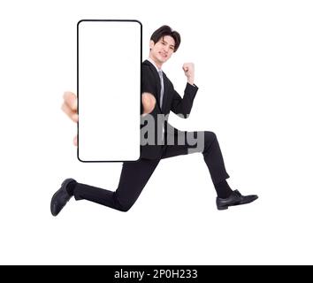 Felice giovane uomo d'affari che salta e mostra lo schermo vuoto del telefono cellulare Foto Stock