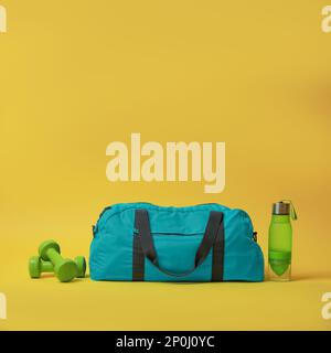 Borsa da palestra blu e accessori sportivi su sfondo giallo Foto Stock