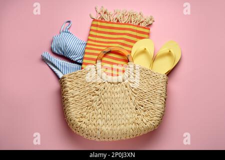 Borsa da spiaggia con asciugamano, costume da bagno e infradito su sfondo rosa, vista dall'alto Foto Stock