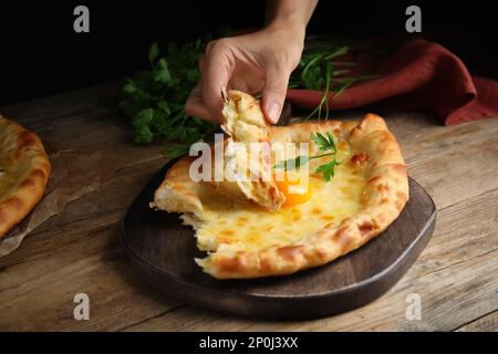 Donna che mangia delizioso Khachapuri Adjarian al tavolo di legno, primo piano Foto Stock