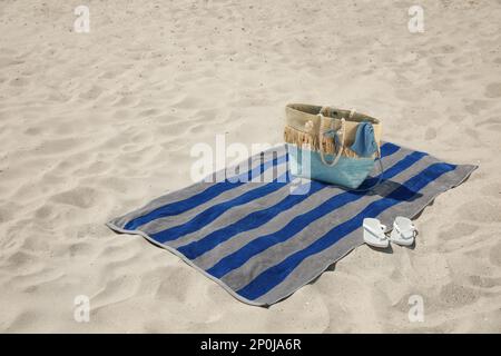 Telo da spiaggia con borsa, infradito e costume da bagno sulla sabbia Foto Stock