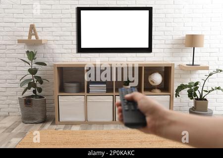 Giovane uomo che cambia canale sul televisore con telecomando a casa, primo piano Foto Stock