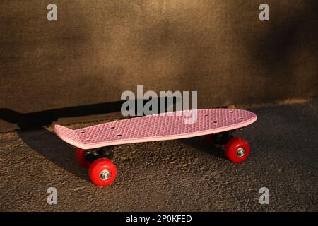 Moderno skateboard rosa con ruote rosse vicino alle pareti nere all'aperto Foto Stock