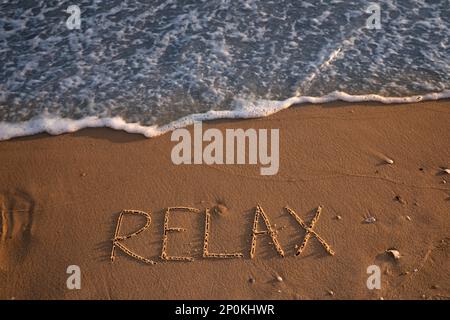 Onde di mare che si arrotolano sulla spiaggia sabbiosa con parola scritta relax, vista dall'alto Foto Stock