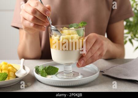 Donna che mangia deliziosa pana cotta con mango a tavola, primo piano Foto Stock