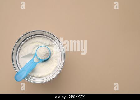 Vista dall'alto di latte in polvere per neonati con scoop in lattina su sfondo beige, spazio per il testo. Latte per bambini Foto Stock