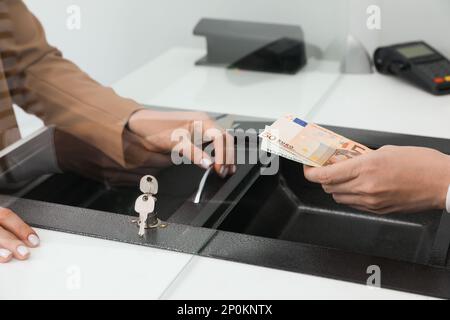 Uomo che dà denaro al cassiere in banca, primo piano. Cambio valuta Foto Stock