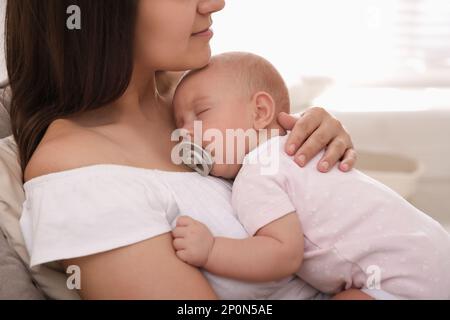 Giovane madre felice con il suo bambino che dorme sulla sedia a casa, primo piano Foto Stock