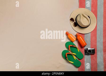 Telo da spiaggia, cappello, occhiali da sole, macchina fotografica, crema solare e infradito sulla sabbia, giacitura piatta. Spazio per il testo Foto Stock