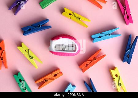 Coloratissimi clothespins e affilatore su sfondo rosa, piatto. Concetto di diversità Foto Stock