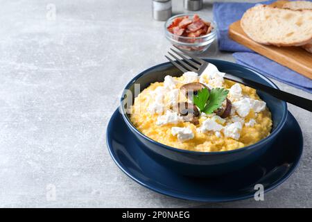 Gustoso banosh servito con brynza e funghi sul tavolo grigio, spazio per il testo. Piatto tradizionale ucraino Foto Stock
