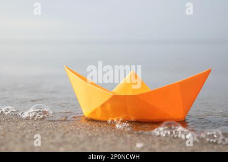 Barca di carta arancione sulla spiaggia di sabbia vicino al mare, primo piano Foto Stock