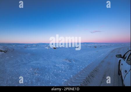 Un paesaggio ghiacciato da un'auto 4x4 su una strada completamente innevata con le gomme che raggiungono l'orizzonte con una magica alba islandese viola. La luce di da Foto Stock