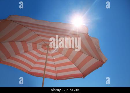 Ombrello da spiaggia a strisce rosse e bianche contro il cielo blu nelle giornate di sole Foto Stock