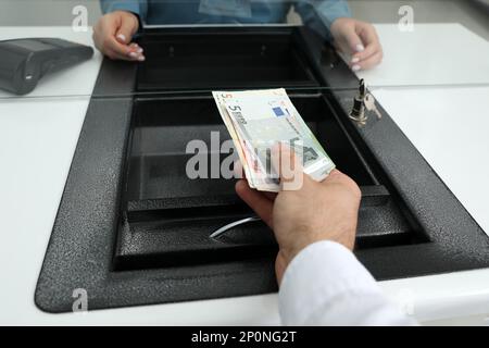 Cassiere che dà denaro a una donna alla finestra di cambio valuta in banca, primo piano Foto Stock