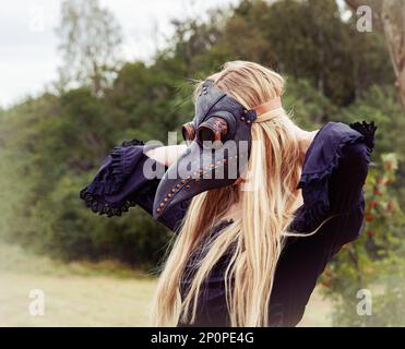 Una foto inquietante e surreale di una donna in una maschera corvo in piedi in un campo. Foto Stock