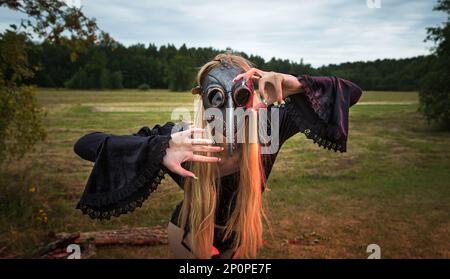 Una foto affascinante e surreale di una donna in una maschera di corvo tra un campo e una foresta. Foto Stock