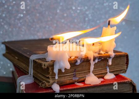 4 candele che bruciano con cera gocciolante sui libri della cover dura dell'annata, primo piano morbido del fuoco Foto Stock
