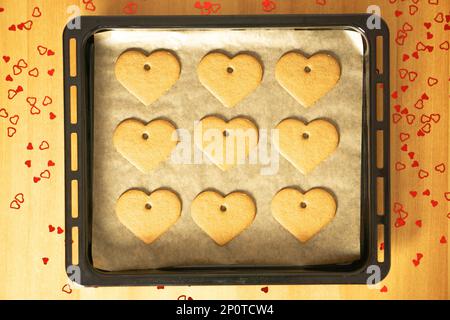 Biscotti romantici al cuore su una teglia da forno sul tavolo con molte decorazioni a cuore rosso. Foto Stock