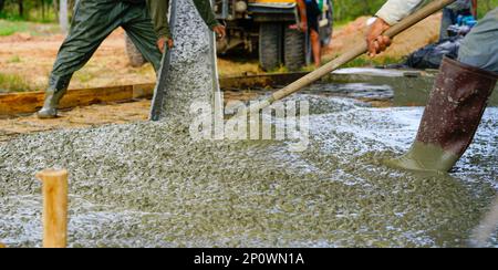 Il lavoratore di costruzione versa calcestruzzo bagnato in cantiere. Addetto alle costruzioni che lavora con il getto di calcestruzzo precompresso da un autocarro per betoniera. Foto Stock