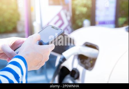 Donna che utilizza il servizio di pagamento tramite smartphone nell'app mobile sulla ricarica di auto EV Blur presso la stazione di ricarica per veicoli elettrici. Punto di ricarica per auto EV. Veicoli commerciali Foto Stock