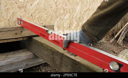 livello rosso nella mano del costruttore quando si utilizza nella costruzione di un oggetto in legno in campagna, un utensile di misurazione di lavoro di un falegname Foto Stock